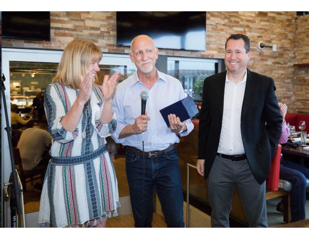 Brent Martini speaking with a microphone at a recognition event, standing between two colleagues